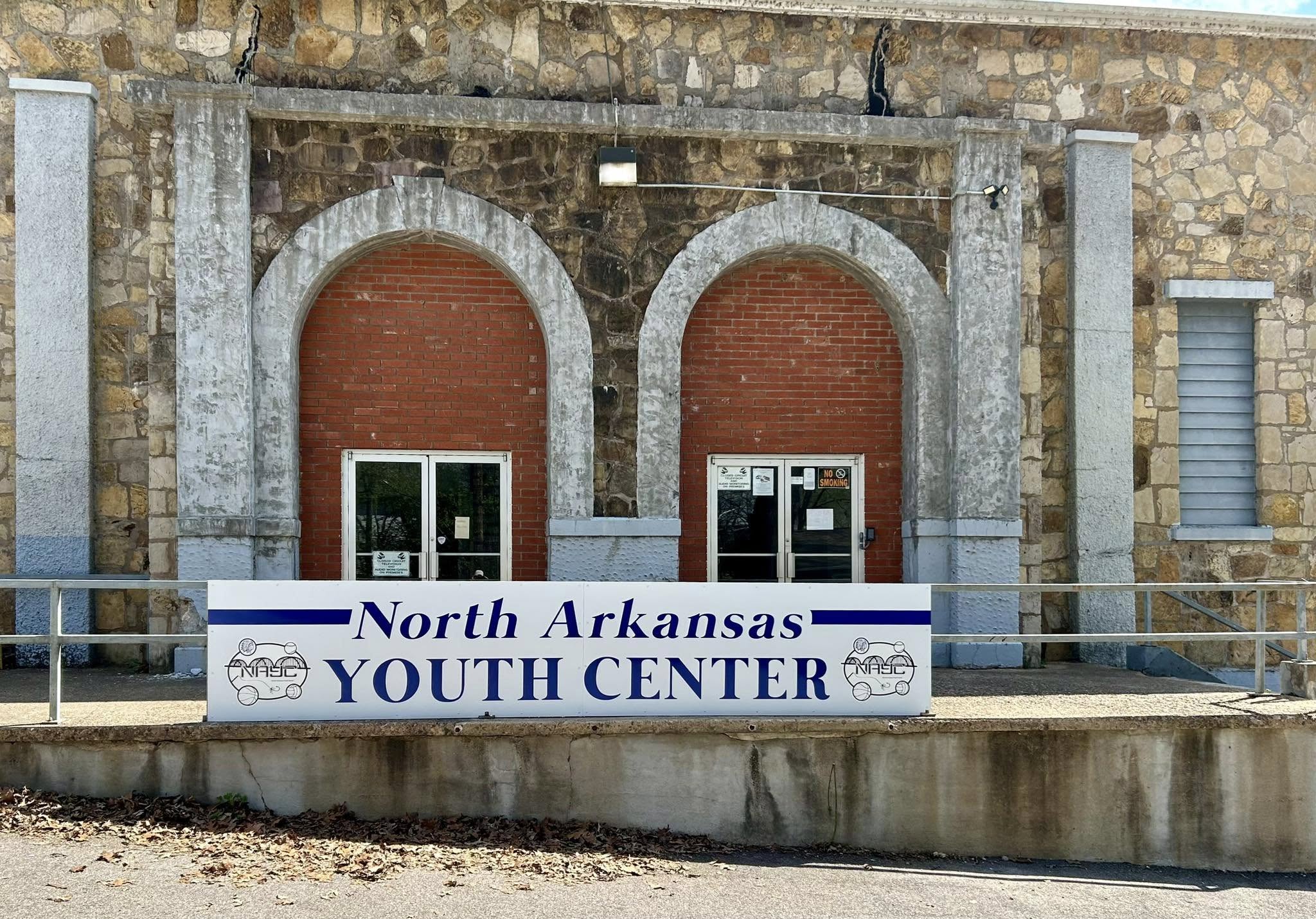 Outdoor building sign for North Arkansas Youth Center, blue text on white panel.