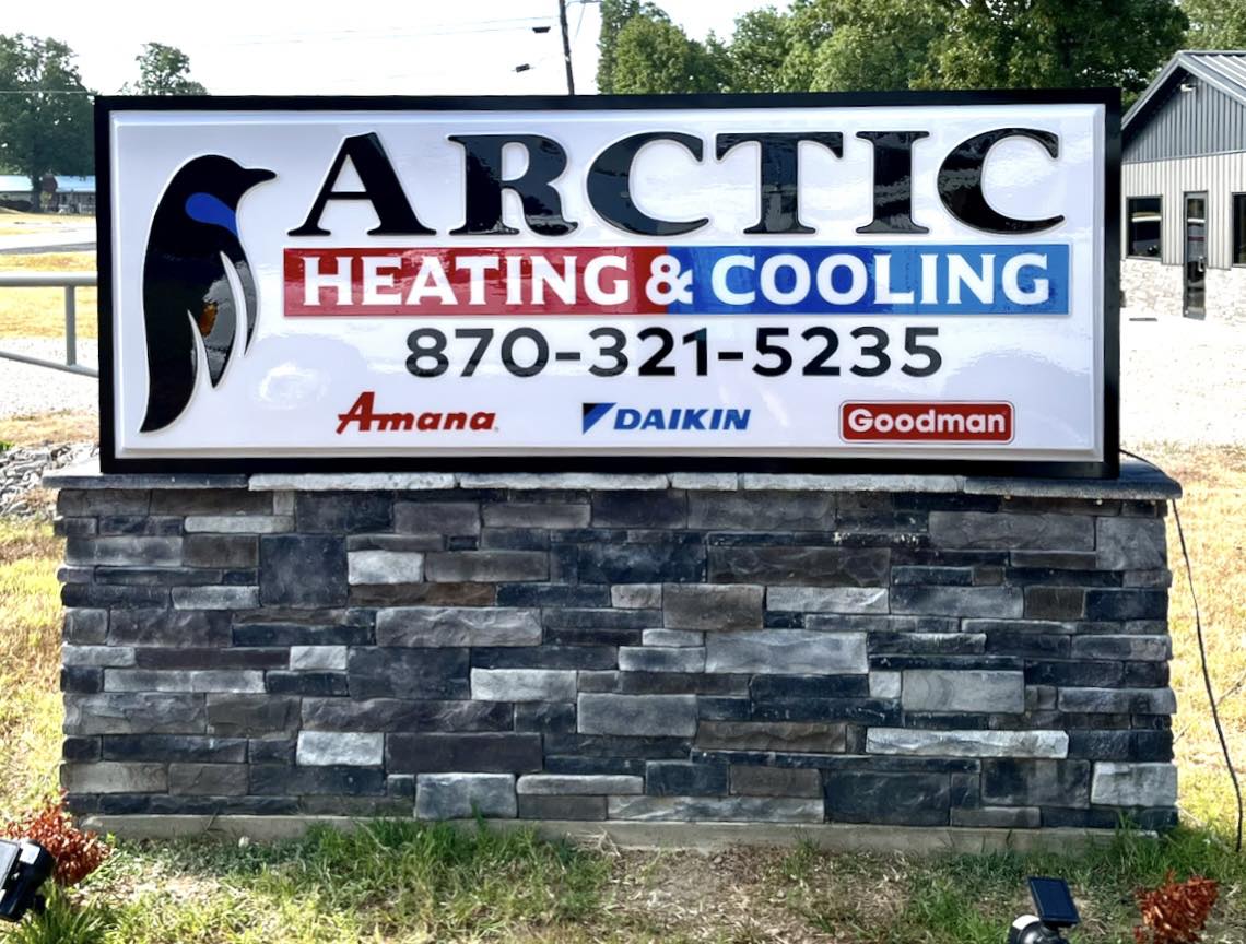 Illuminated monument sign on a stone base for Arctic Heating & Cooling, featuring a penguin logo.