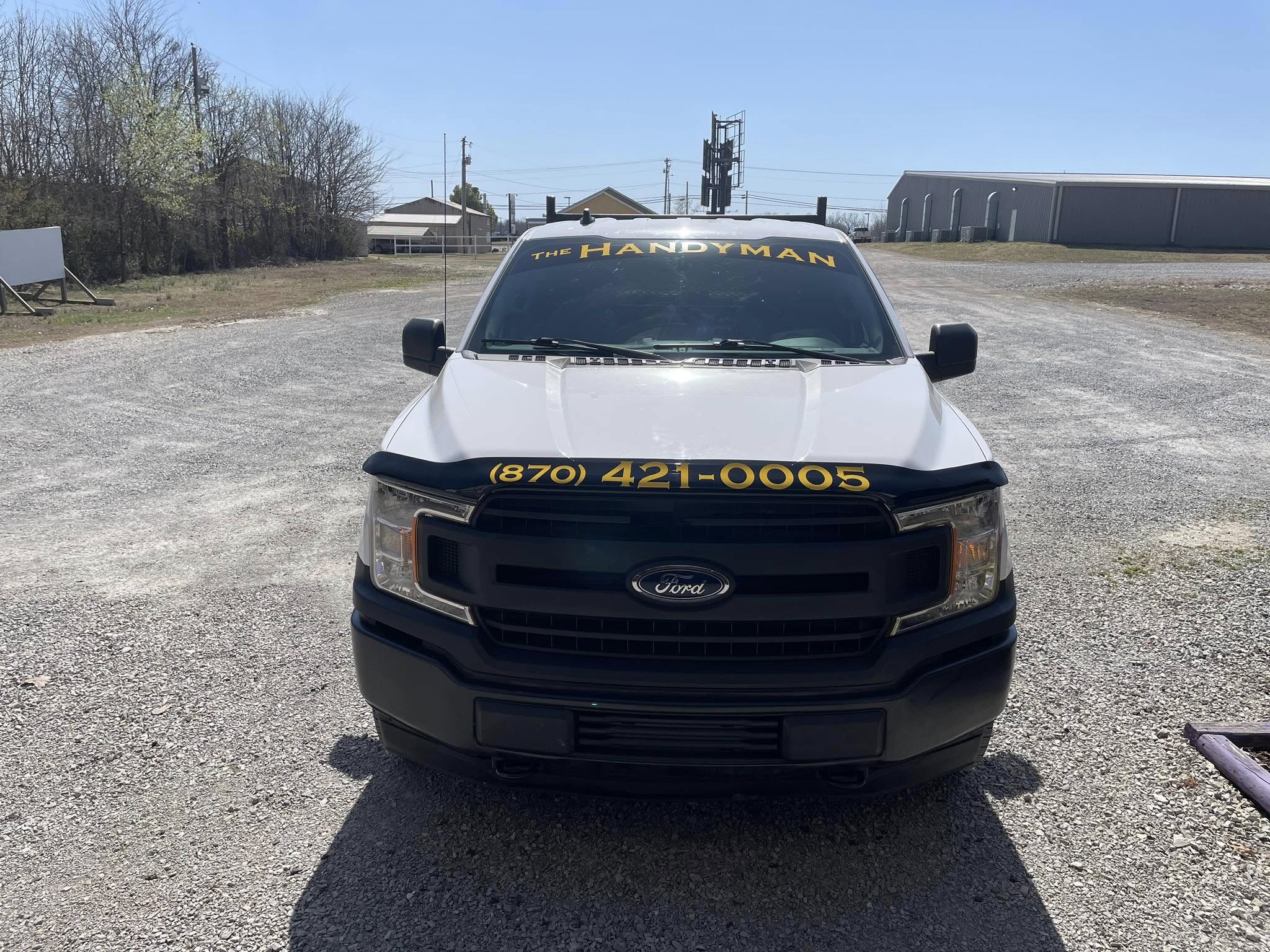 White Ford F-150 with yellow "The Handyman" windshield banner and phone number decal.