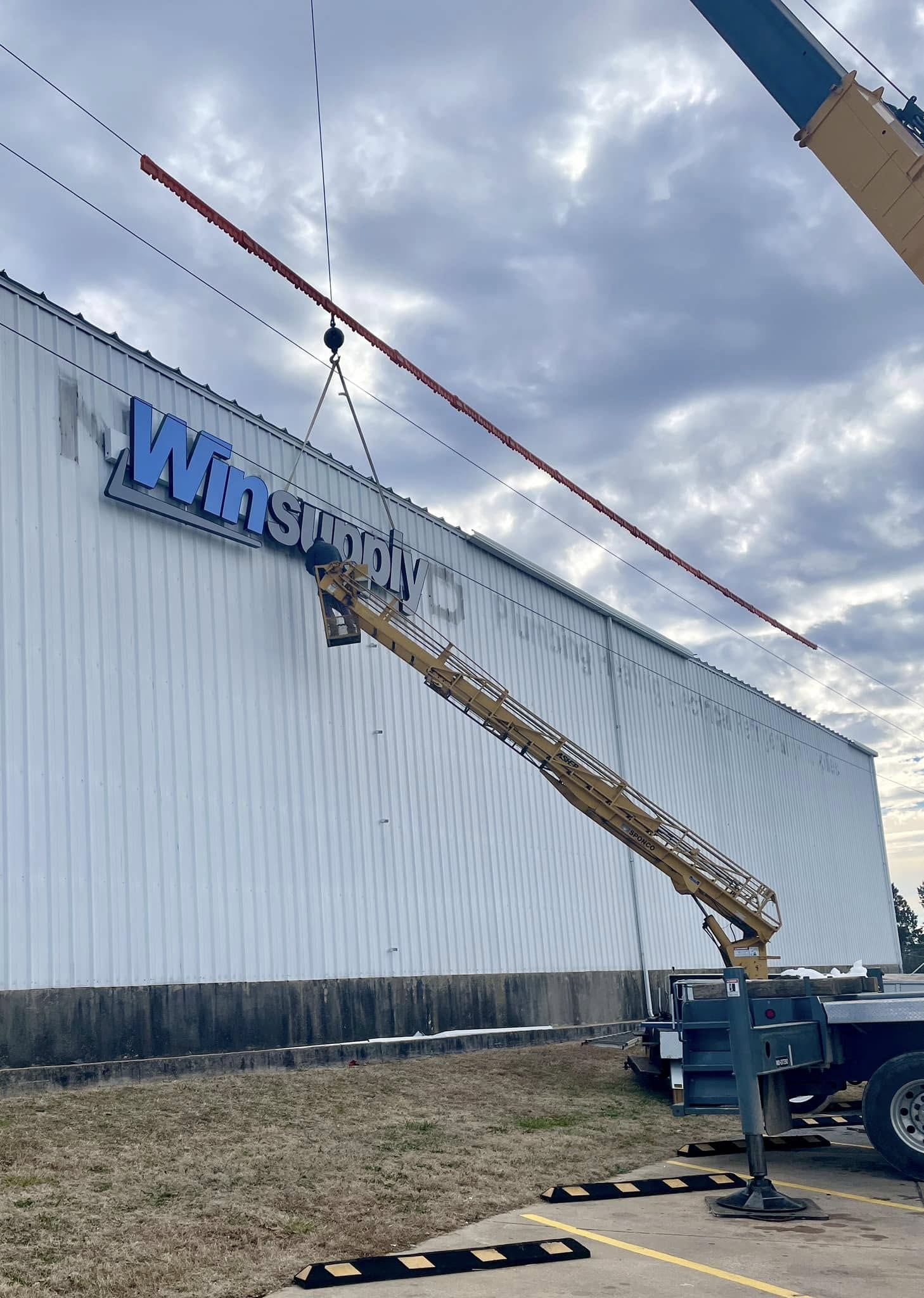 Installation of large blue and gray channel letters spelling 'Winsupply' on a white corrugated building.