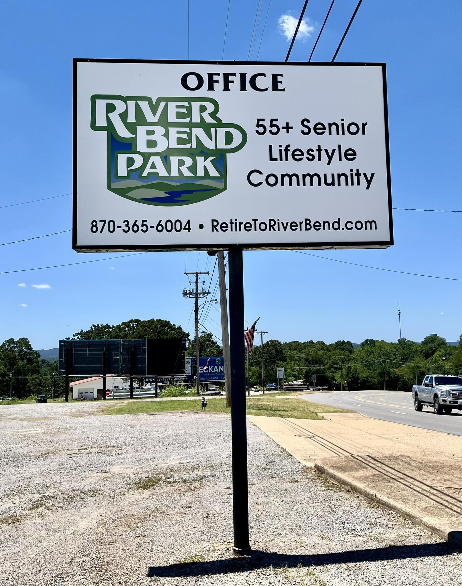 White pylon sign with green and blue River Bend Park logo, contact info, and '55+ Senior Lifestyle Community' text.