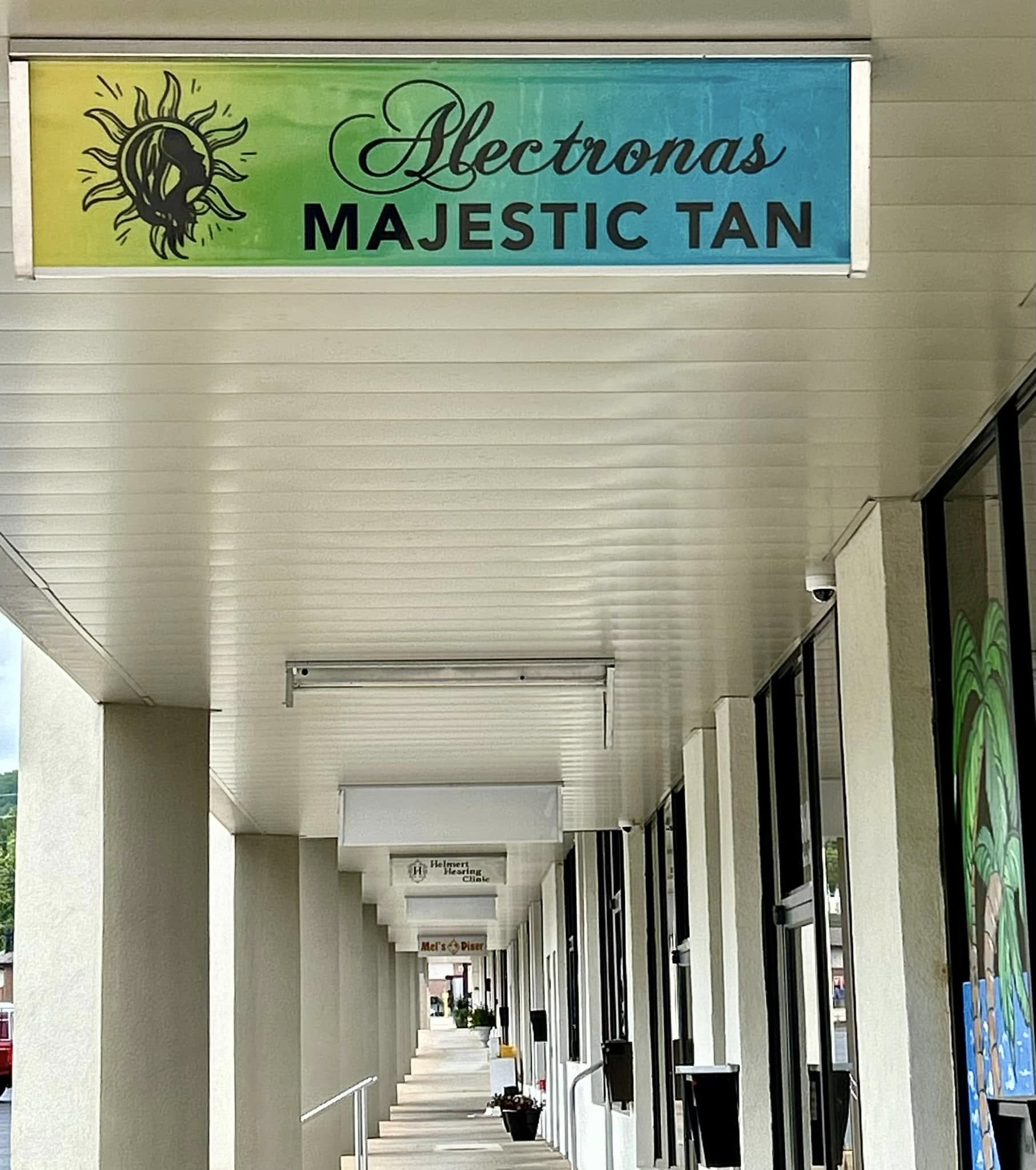 Illuminated storefront sign for Alectronas Majestic Tan with sun logo and gradient background.