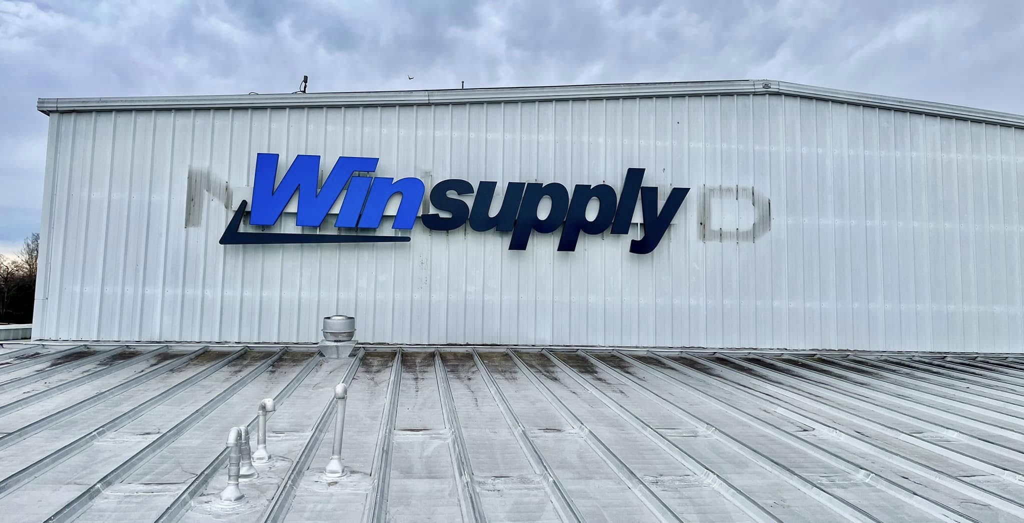 Blue dimensional letter sign for Winsupply on gray corrugated metal building facade