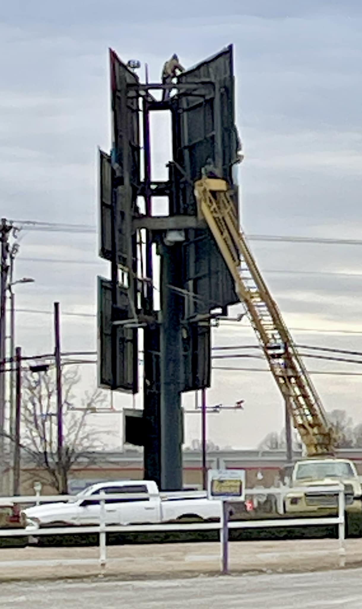 Sign installer working on replacing panels of a very tall monument sign with a lifted crane.