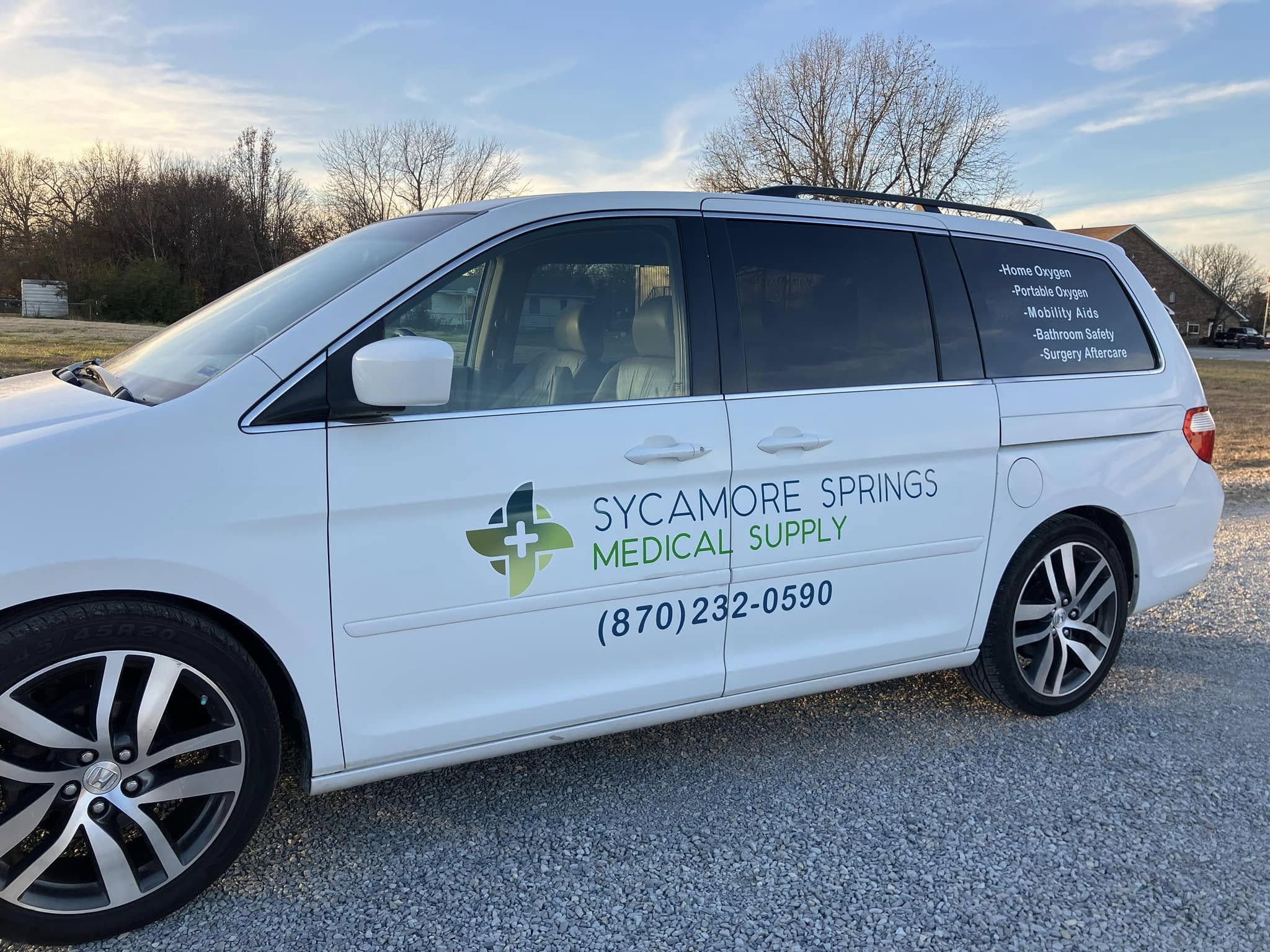 White minivan with vinyl graphics for Sycamore Springs Medical Supply, including logo and contact information.