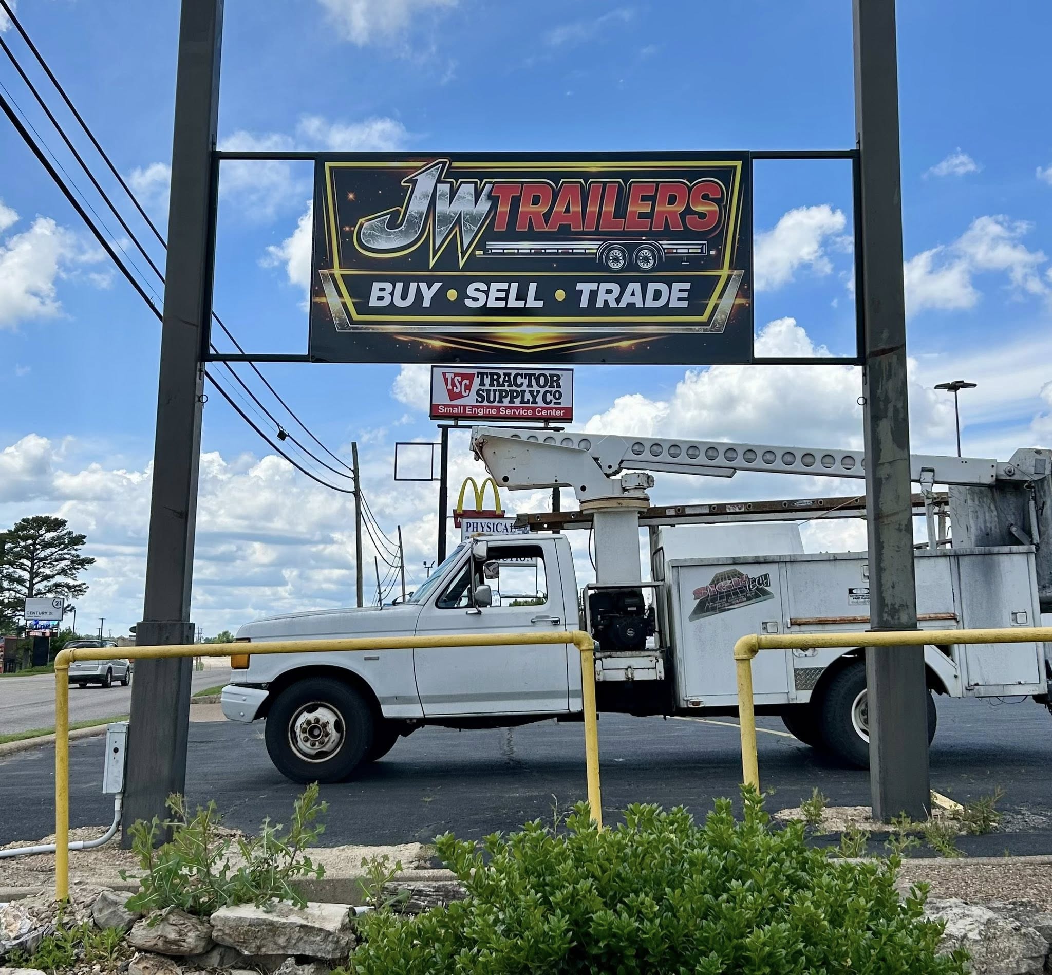 A large black outdoor sign for JW Trailers, reading "Buy Sell Trade" mounted on a tall grey pole.