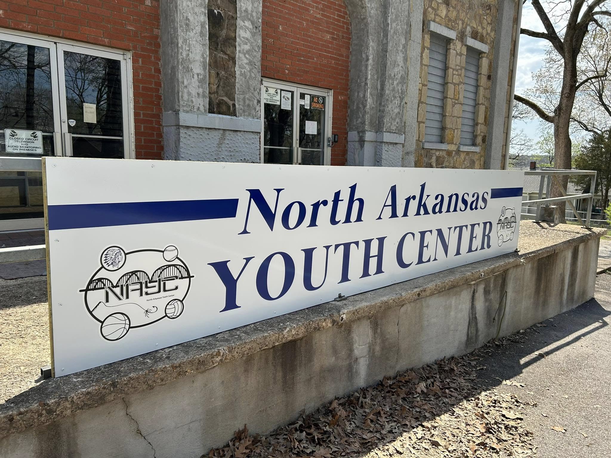 North Arkansas Youth Center sign, white panel with blue text, free-standing on stone wall.