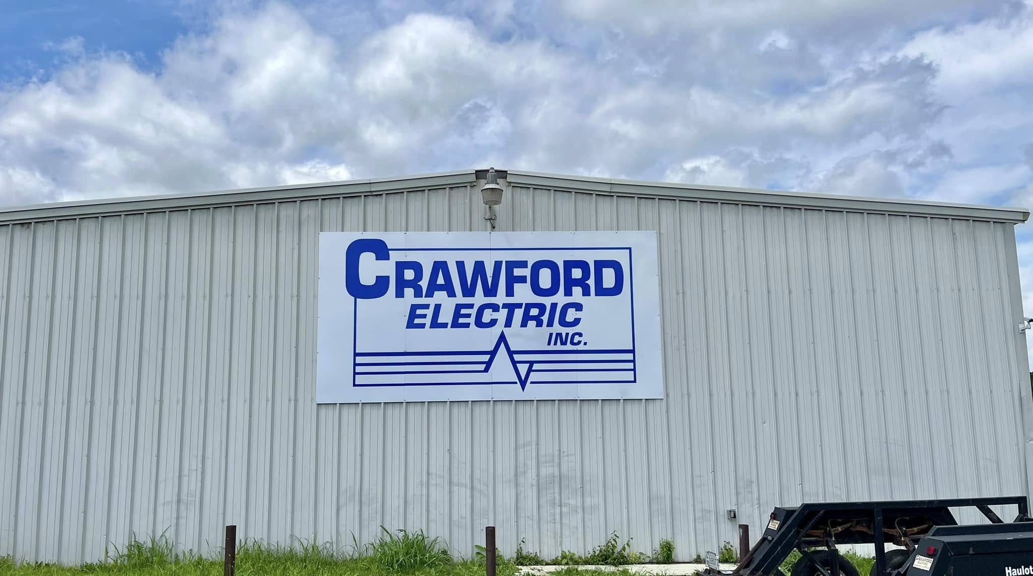 A large blue and white Crawford Electric Inc. sign on the side of a grey corrugated metal building.