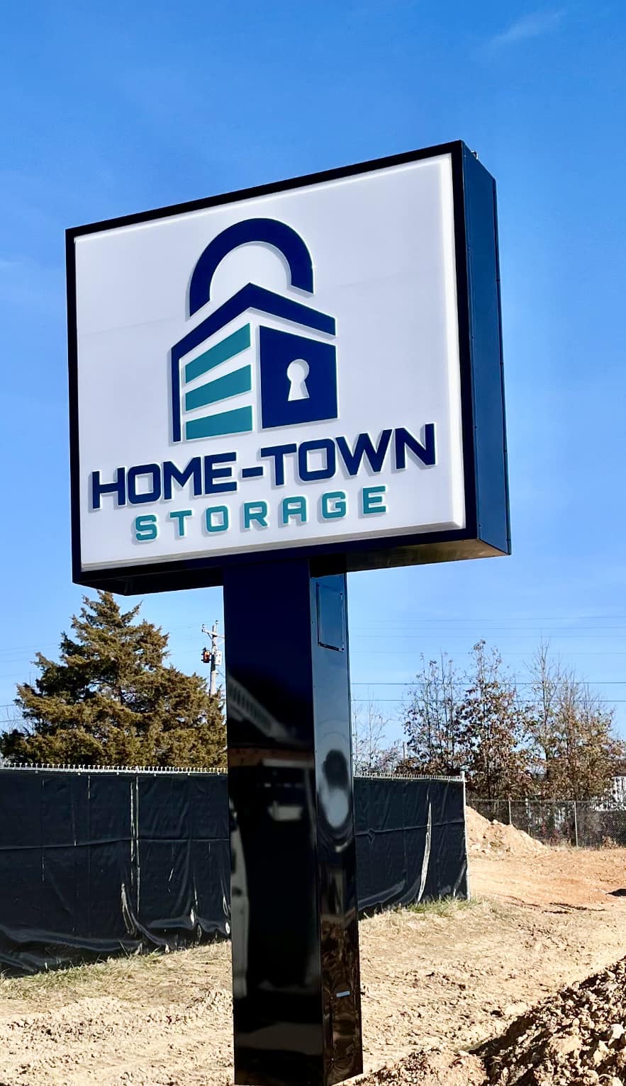 Tall pylon sign with an illuminated box for Home-Town Storage, featuring a lock and building logo.