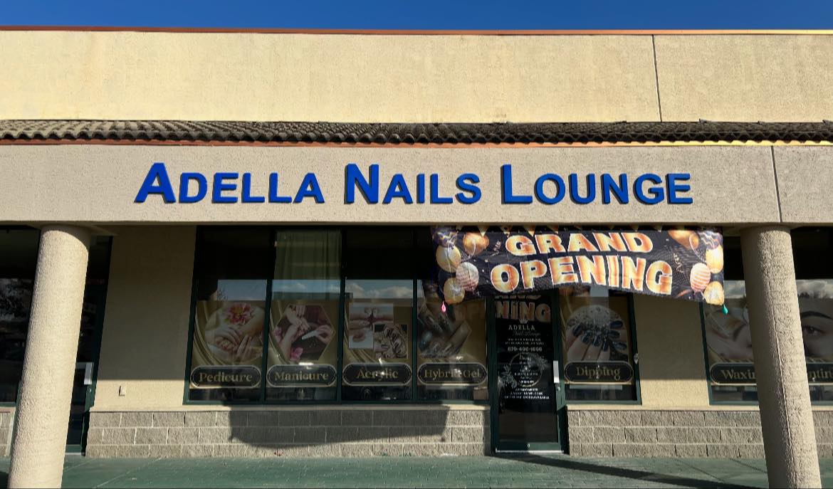 Blue dimensional letters spelling 'Adella Nails Lounge' mounted on a textured building facade above a storefront.