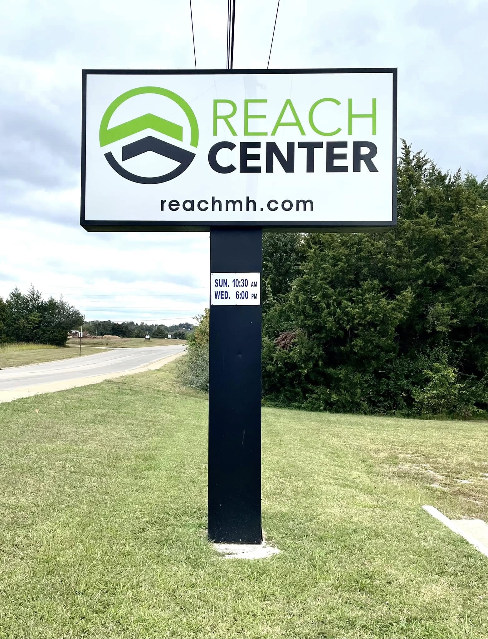 White and black monument sign for Reach Center with green logo and website.