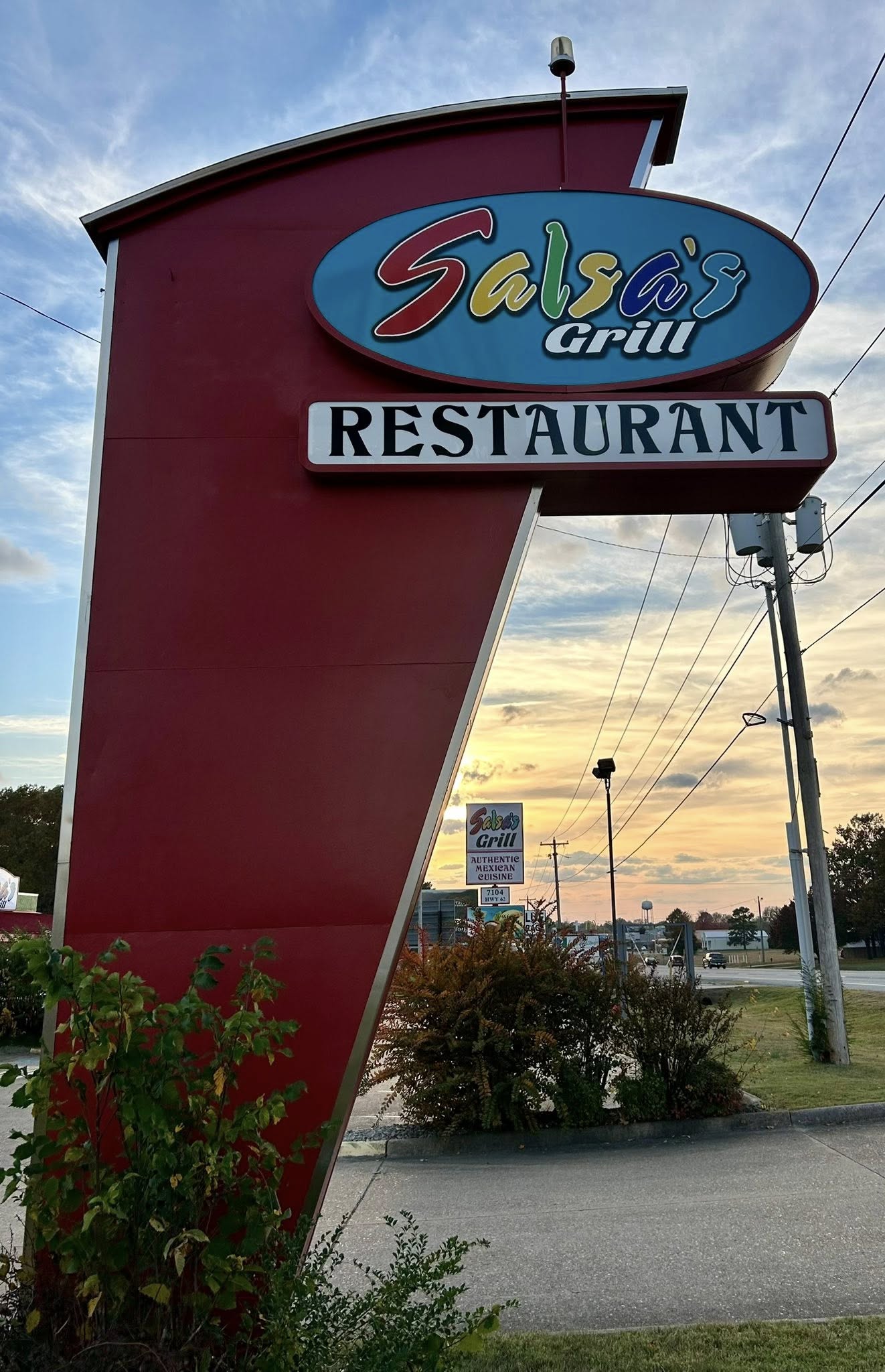 Red pylon sign for Salsa's Grill Restaurant featuring colorful brand logo against a sunset sky.
