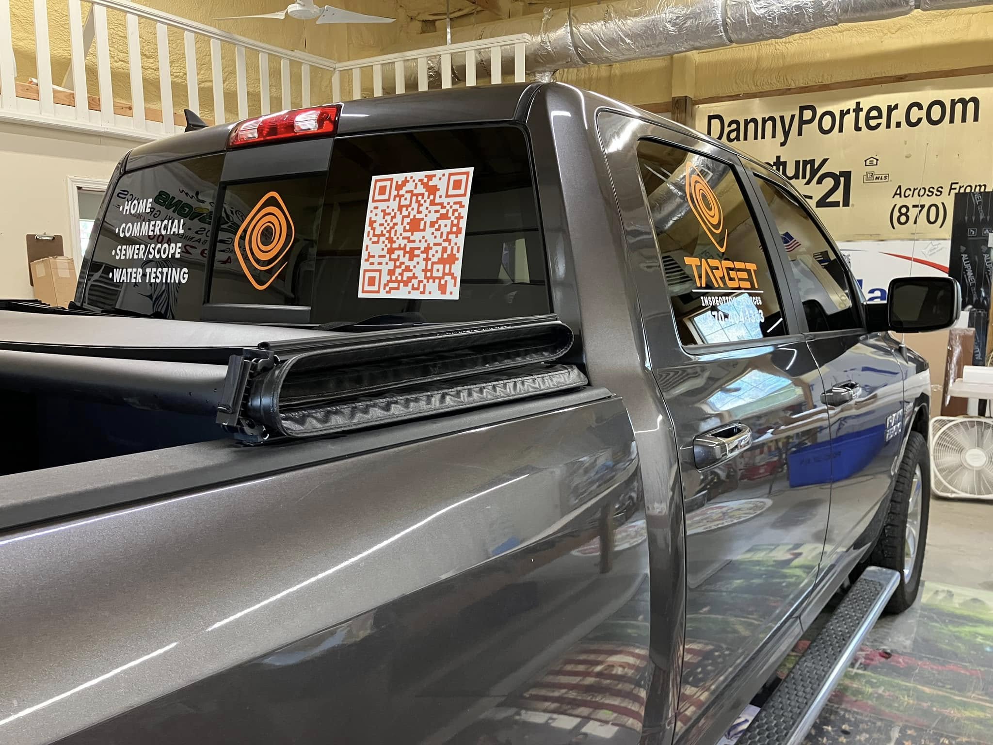 Orange logos and white text decals, including a QR code, on the windows of a grey pickup truck.
