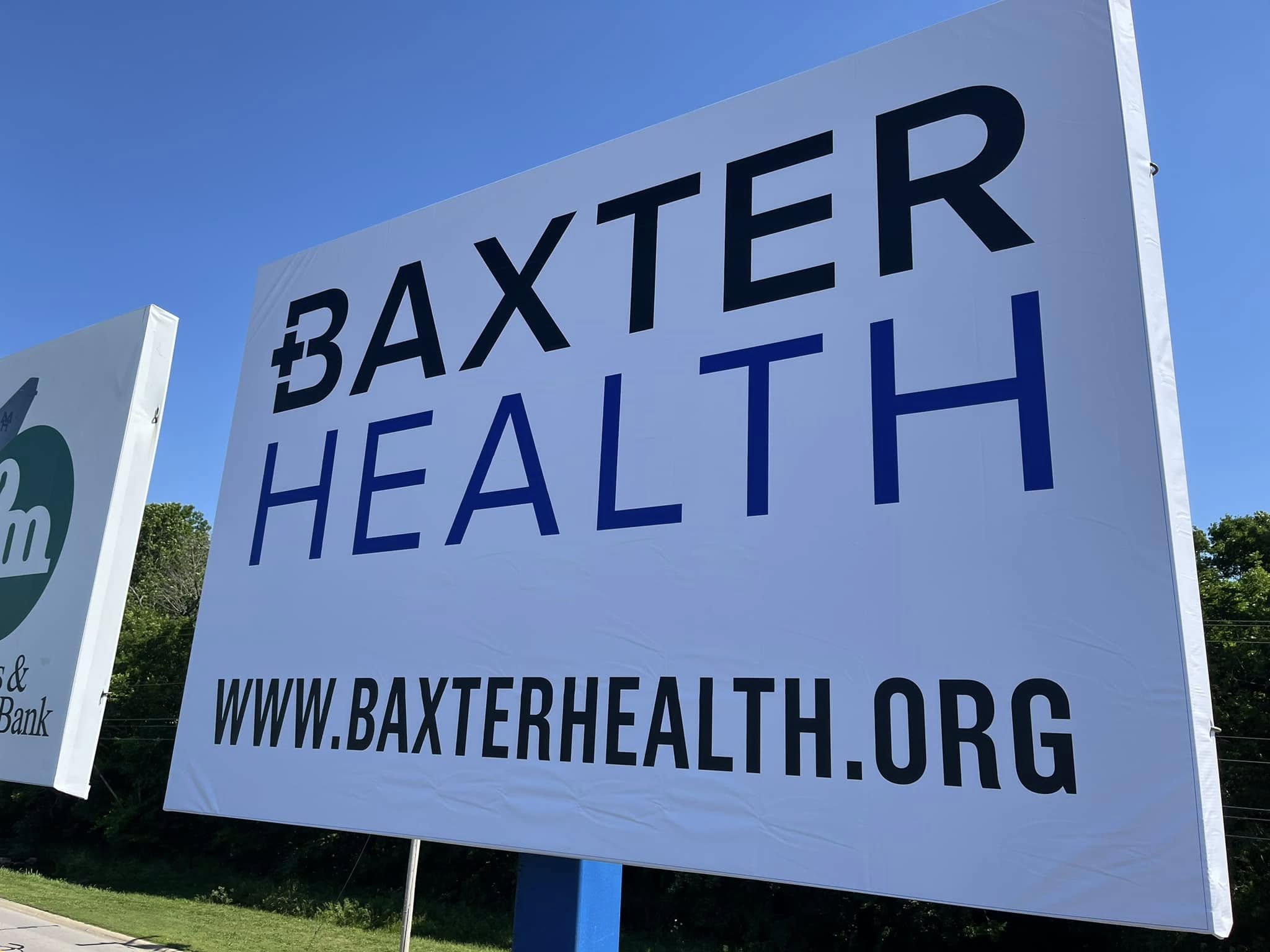 Large white banner sign for Baxter Health with black and blue text and website address.