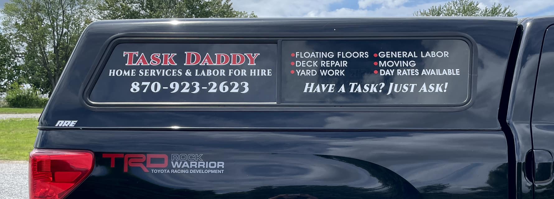 White vinyl window graphics on the rear truck cap of a black utility truck for Task Daddy Home Services