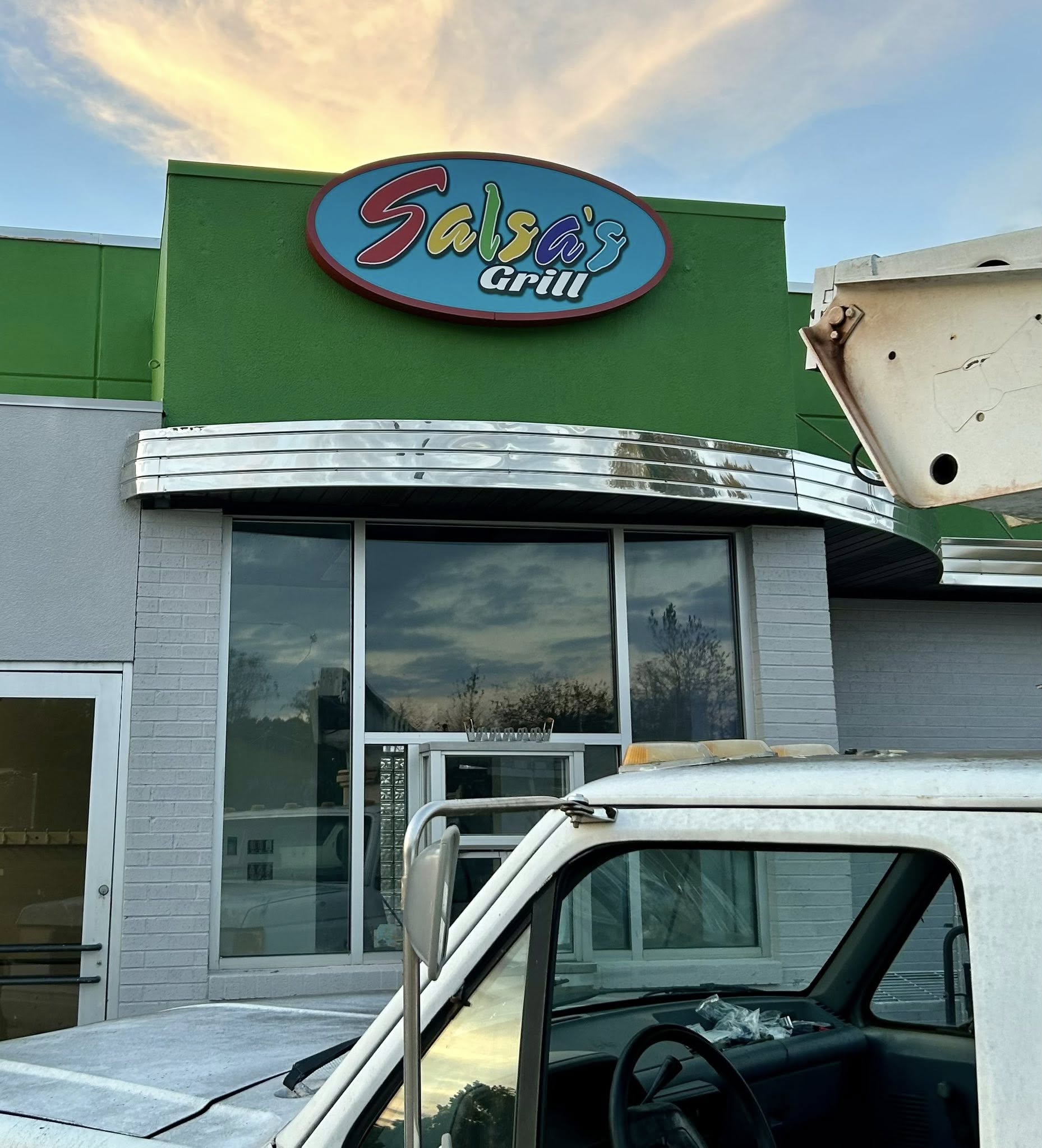 Outdoor illuminated oval sign for Salsa's Grill restaurant on a vibrant green building facade.