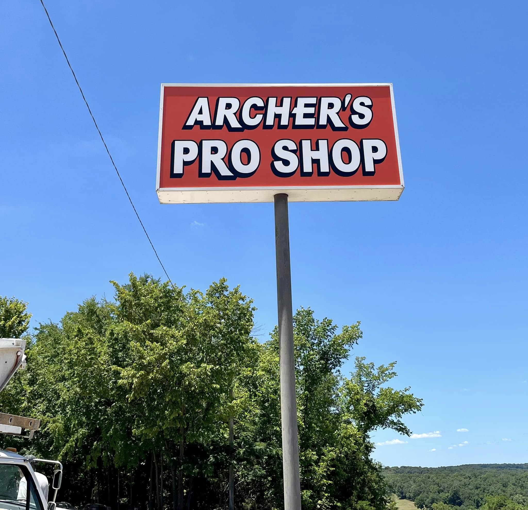 Red pylon sign for Archer's Pro Shop with white lettering against a clear blue sky