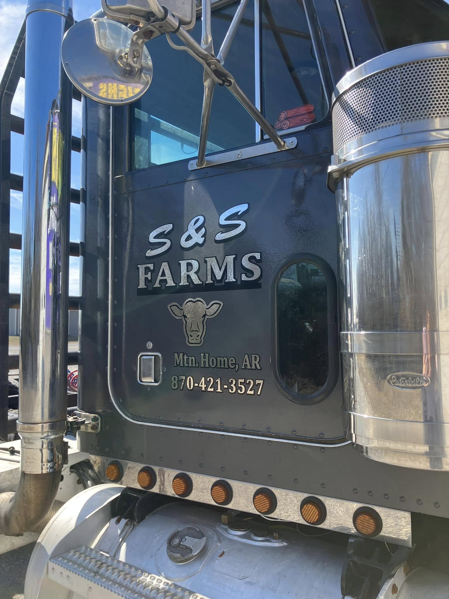 Custom cut vinyl graphics for S&S Farms, including a cow logo, on a black semi-truck.