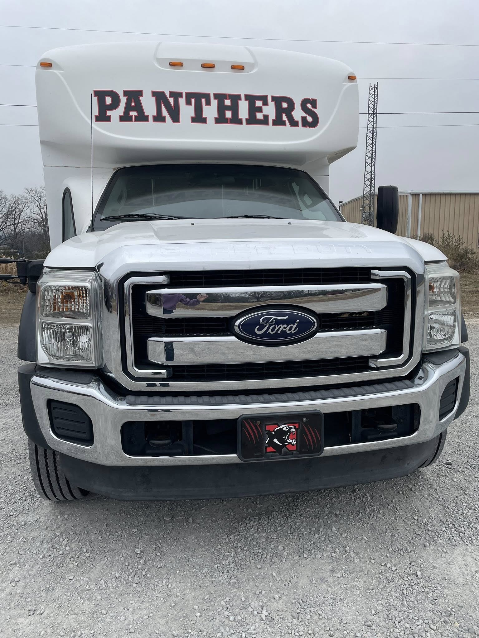 White Ford mini-bus with 'PANTHERS' decals and custom license plate frame for school sports team.