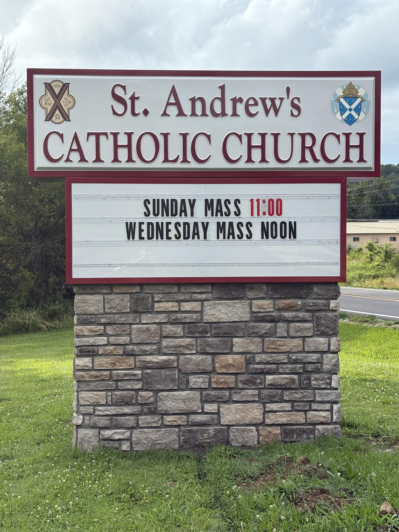 Custom monument sign with brick base for St. Andrew's Catholic Church, displaying mass times.