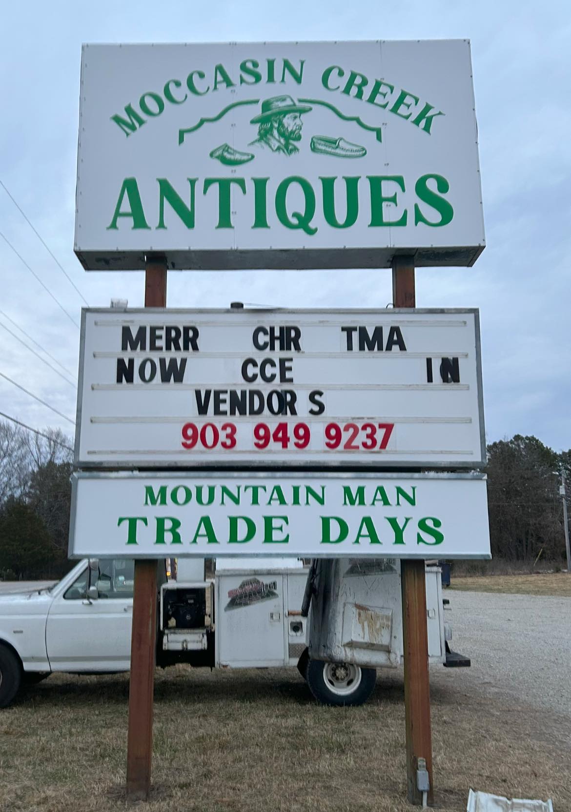 White pylon sign with green lettering for "Moccasin Creek Antiques" and a changeable black letter message board.