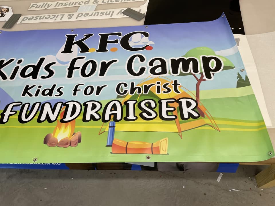 Colorful vinyl banner for KFC Kids for Camp Kids for Christ Fundraiser with camping graphics.