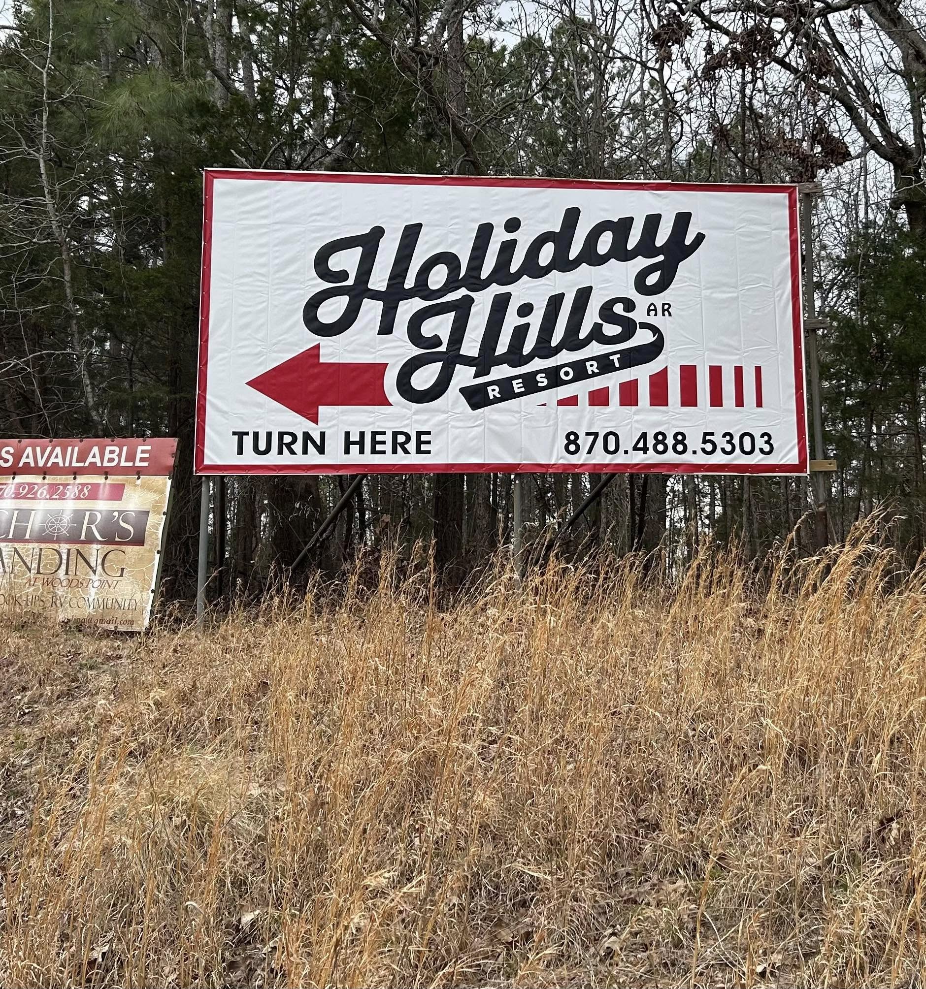 Holiday Hills Resort pylon sign with arrow and phone number in a wooded area.