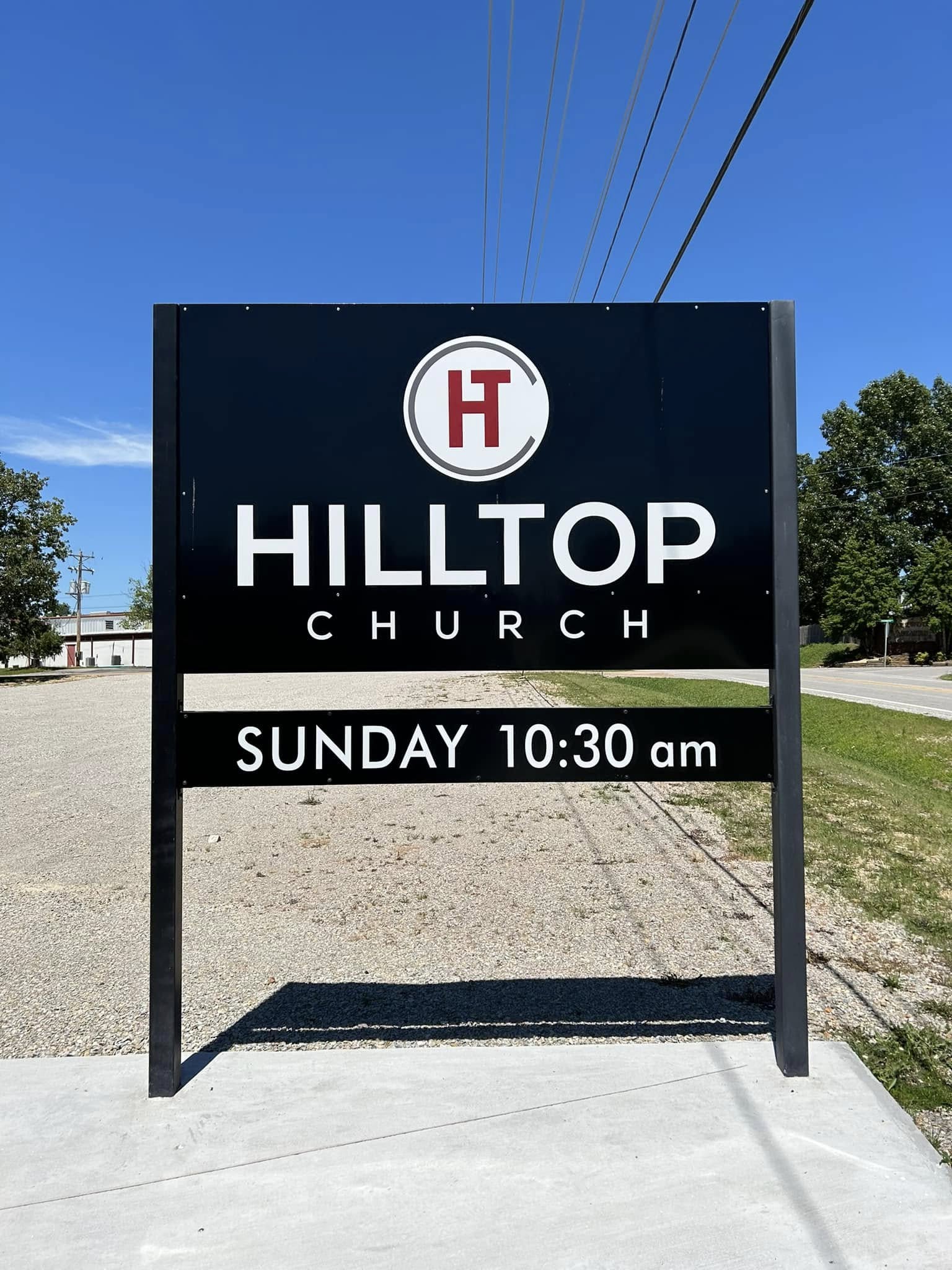 Black Hilltop Church roadside pylon sign with white text and logo, for Sunday service times.