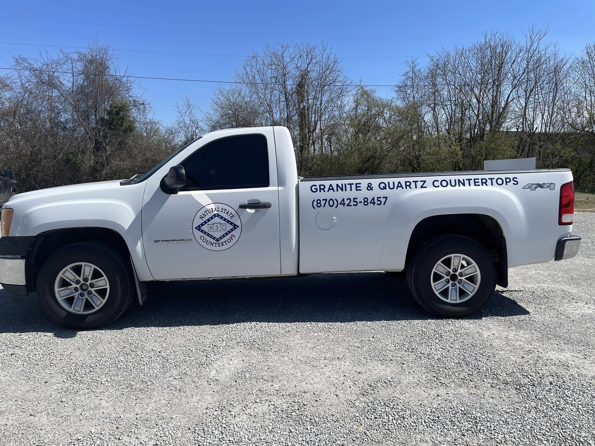 White GMC Sierra pickup truck with blue vinyl graphics for Natural State Countertops.