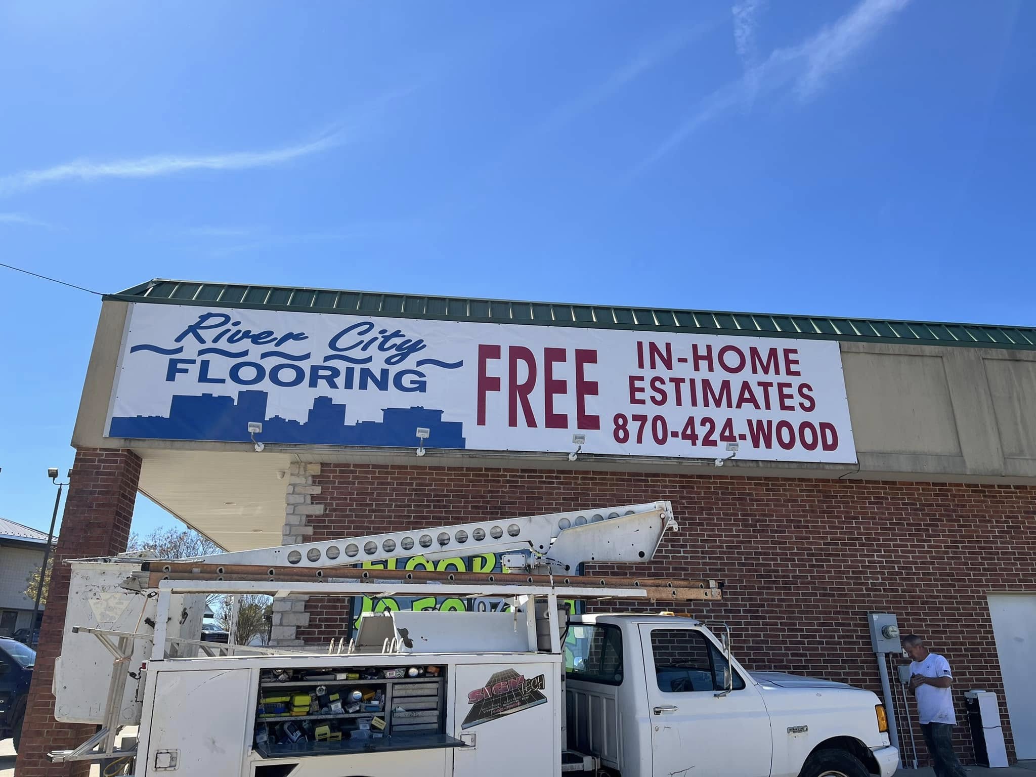 Large vinyl sign for River City Flooring on a brick building facade.