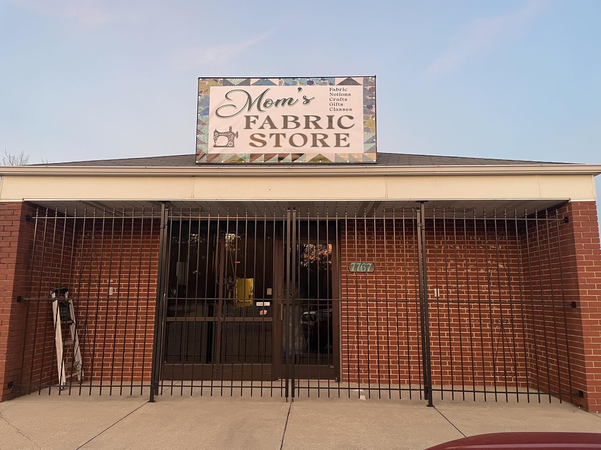 Outdoor banner for Mom's Fabric Store with sewing machine graphic and quilt-pattern border.