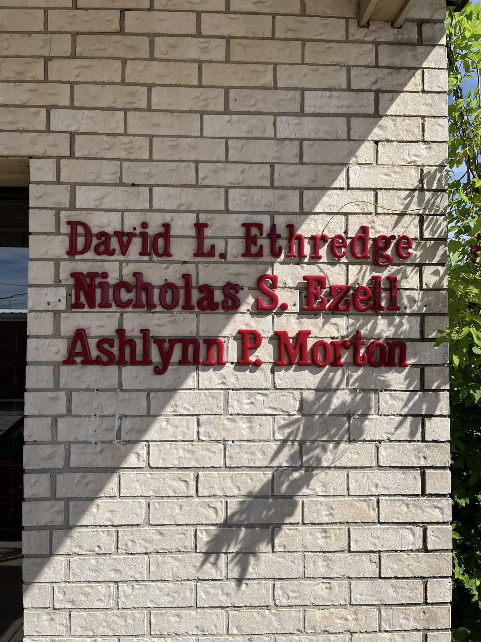 Red dimensional letters spelling out names, mounted on a white brick wall for building identification.